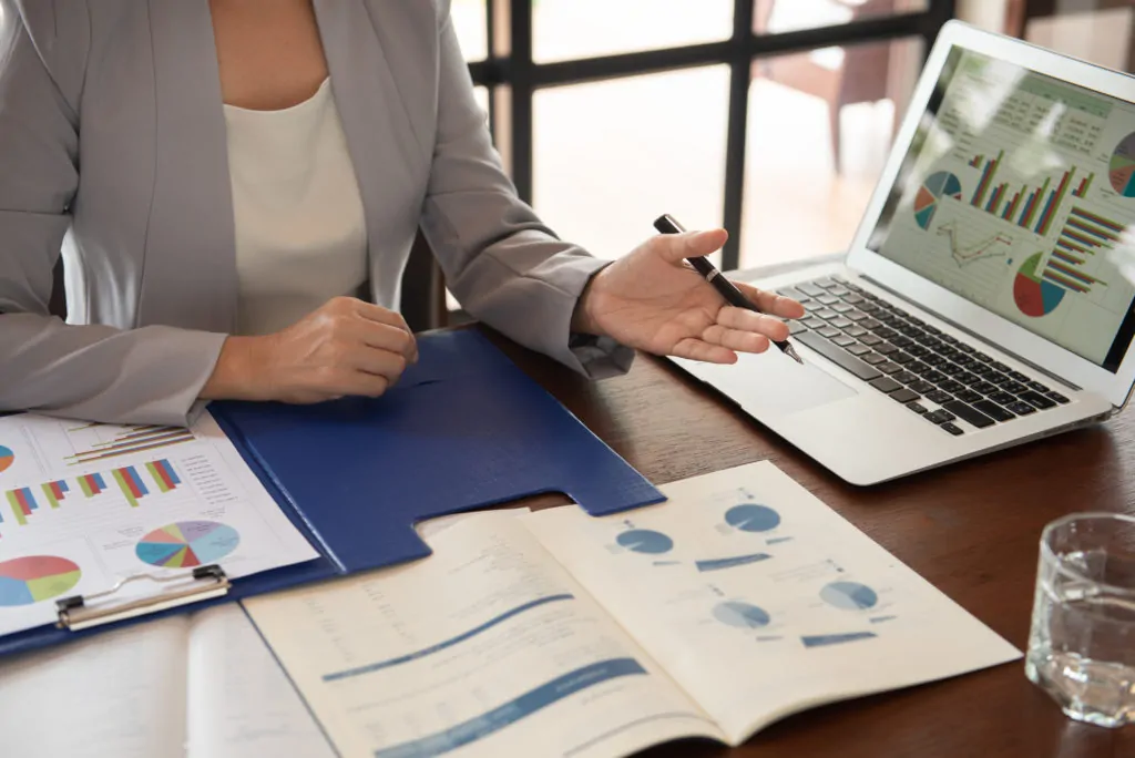 Hands of advisor reviewing data, charts, and graphs on printed documents as well as laptop.