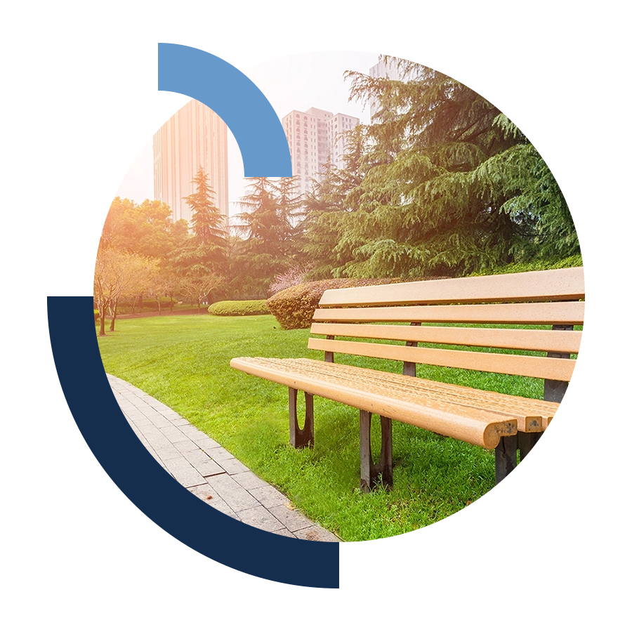 Wooden park bench on green grass facing paved path on a sunny day.