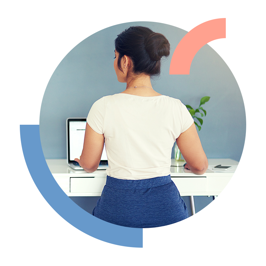 View from behind of woman sitting on balance ball chair at a desk working on a laptop.