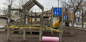 Wooden playground equipment blocked with yellow caution tape on a rainy day.