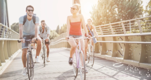 Friends riding bicycles on city park bridge path in Summer.