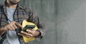 Maintenance worker with hardhat under arm and using mobile phone.