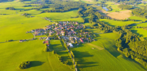 Drone view of small town surrounded by wooded area and green fields.