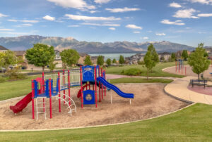 Red and blue playground equipment in residential area with mountain landscape in the background.