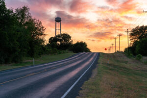 Empty country road at sunset with water tower in the distance.