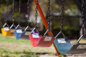 Close up of four coloured swings at a playground.
