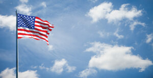 United States flag flying in front of blue sky with white clouds.