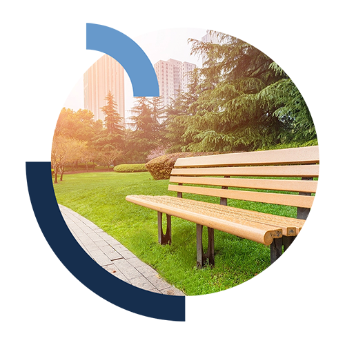 Wooden park bench on green grass facing paved path on a sunny day.