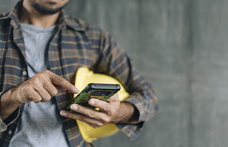 Maintenance worker with hardhat under arm and using mobile phone.