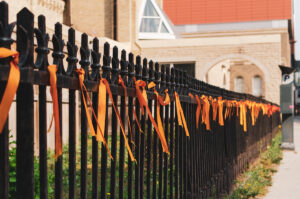 Metal fence with orange ribbons tied to it.