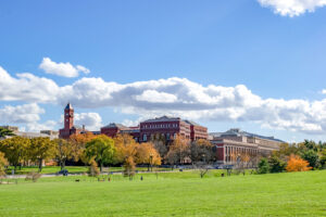 A scenic view of Clemson University's campus in South Carolina, featuring a historic red brick building with a prominent clock tower, surrounded by lush green trees under a clear sky.