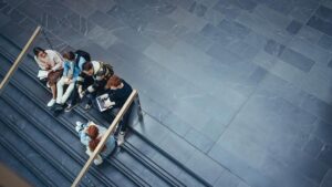 An aerial view of students on the stairs of a university campus, socializing and studying with materials out before them.