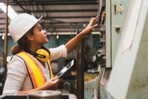 Female engineer with tablet inspecting factory machinery, showing CMMS mobile audit tools for facility compliance.