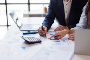 Two colleagues reviewing charts on printed financial reports, with a calculator and laptop on the desk.