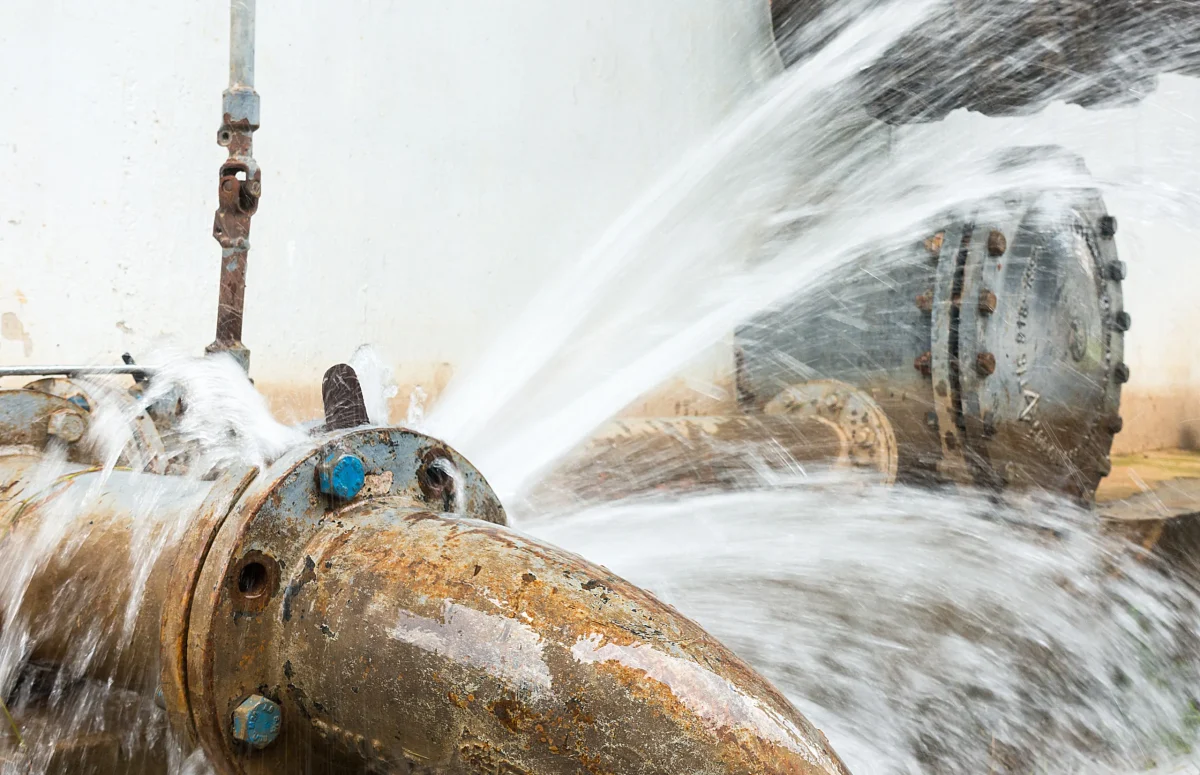 Close up of rusted pipes bursting with water.